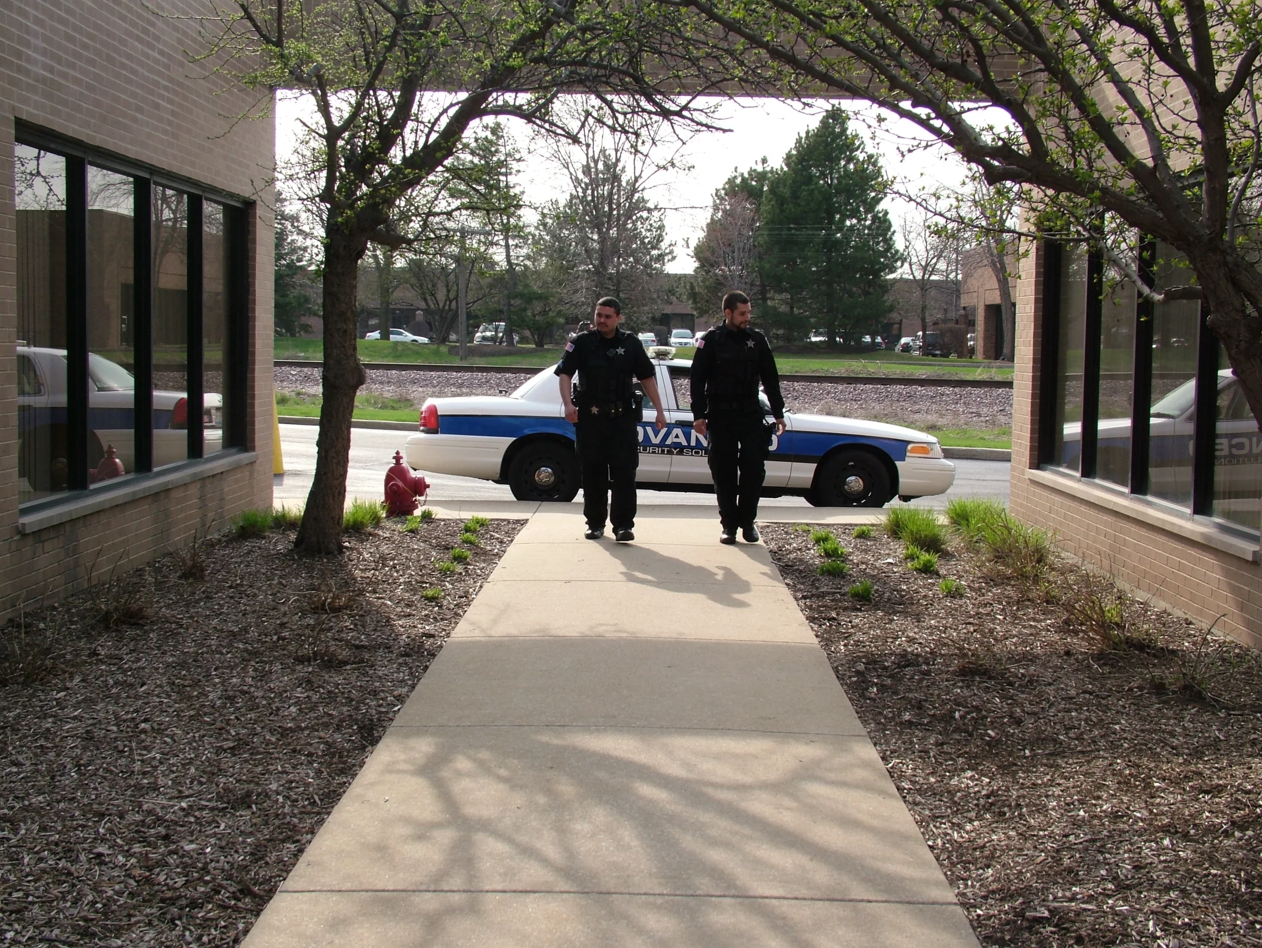 emergency-staffing-chicago-illinois-60656 Two security officers walking a property perimeter with a patrol vehicle in the background