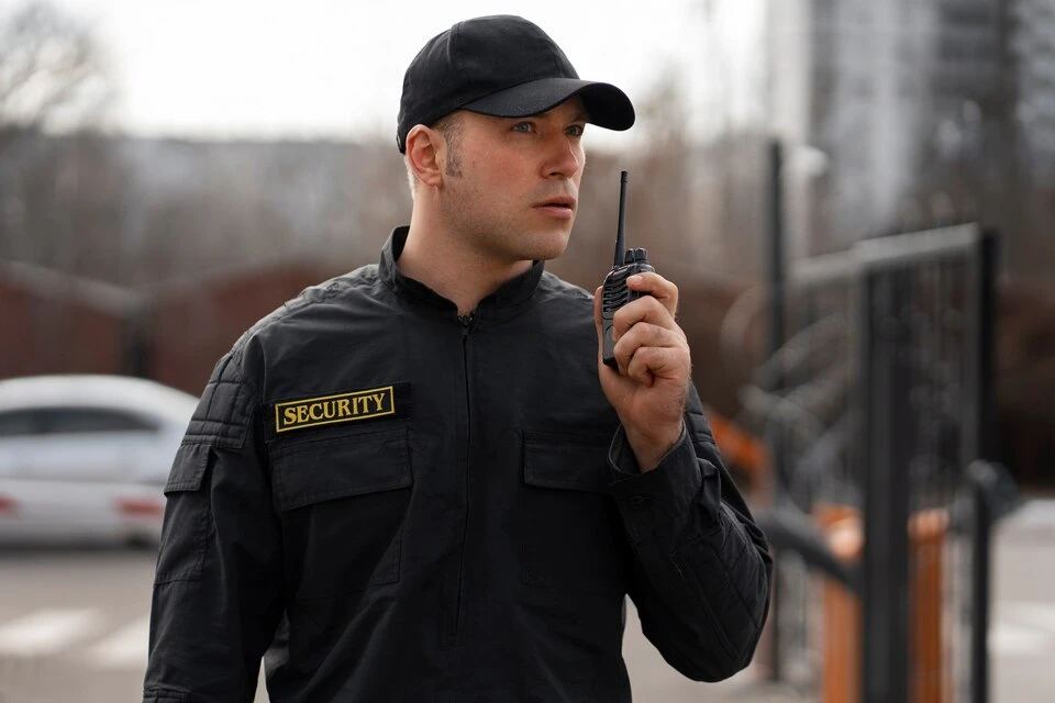Security officer wearing a “SECURITY” jacket speaking into a two-way radio outdoors