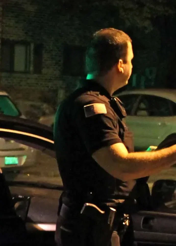 Uniformed security officer beside a vehicle during a nighttime response & lockup patrol for Chicago-area properties.